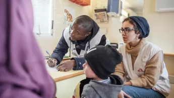 Unsere Kulturelle Vermittlerin Myriam Abdel-Basit und Dr. Yorpoi Bockarie während einer Konsultation im Camp Moria auf Lesbos. Kulturelle Vermittlerin, Arzt und kleiner Patient in Sprechstunde