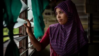 Die gefährliche Fluchtroute vieler Rohingya endet in Malaysia. Eine Frau sitzt im Dunkeln und blickt durch vergitterte Fenster