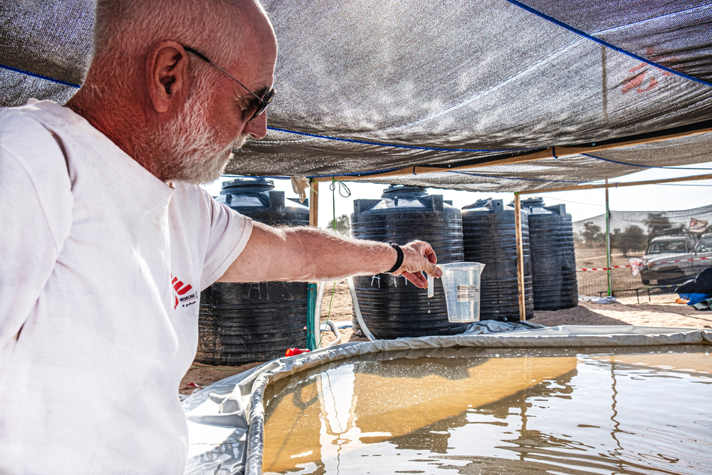 Mitarbeitender hebt Wasser aus Sammelbecken im Camp Metche