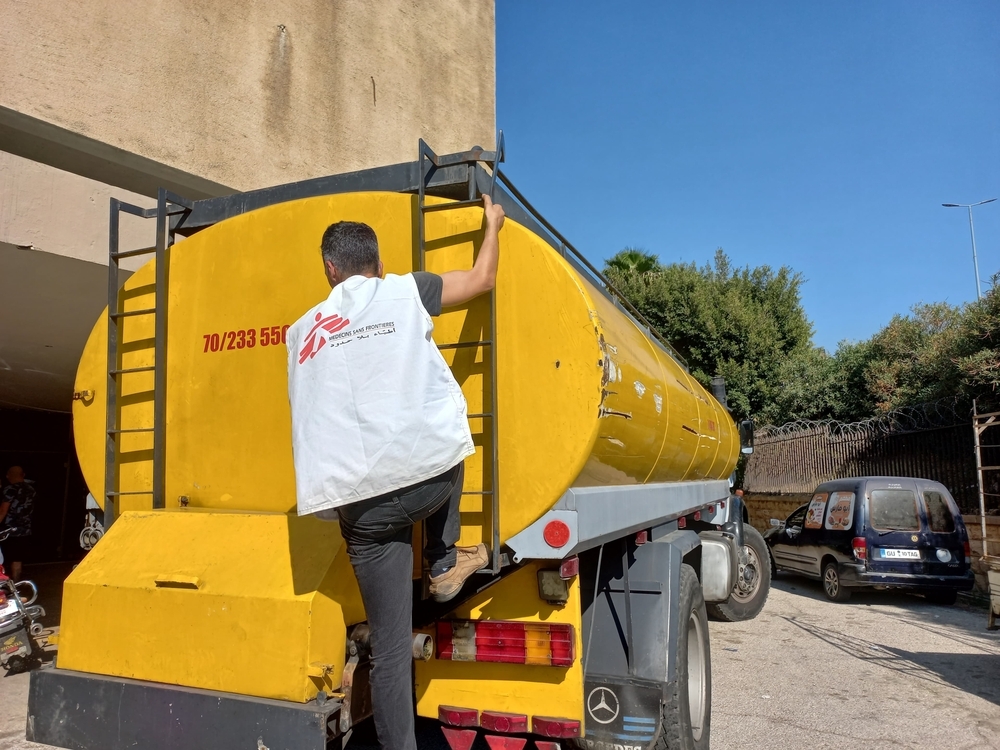 Mitarbeitender steht auf Endteil von gelbem Wassertruck