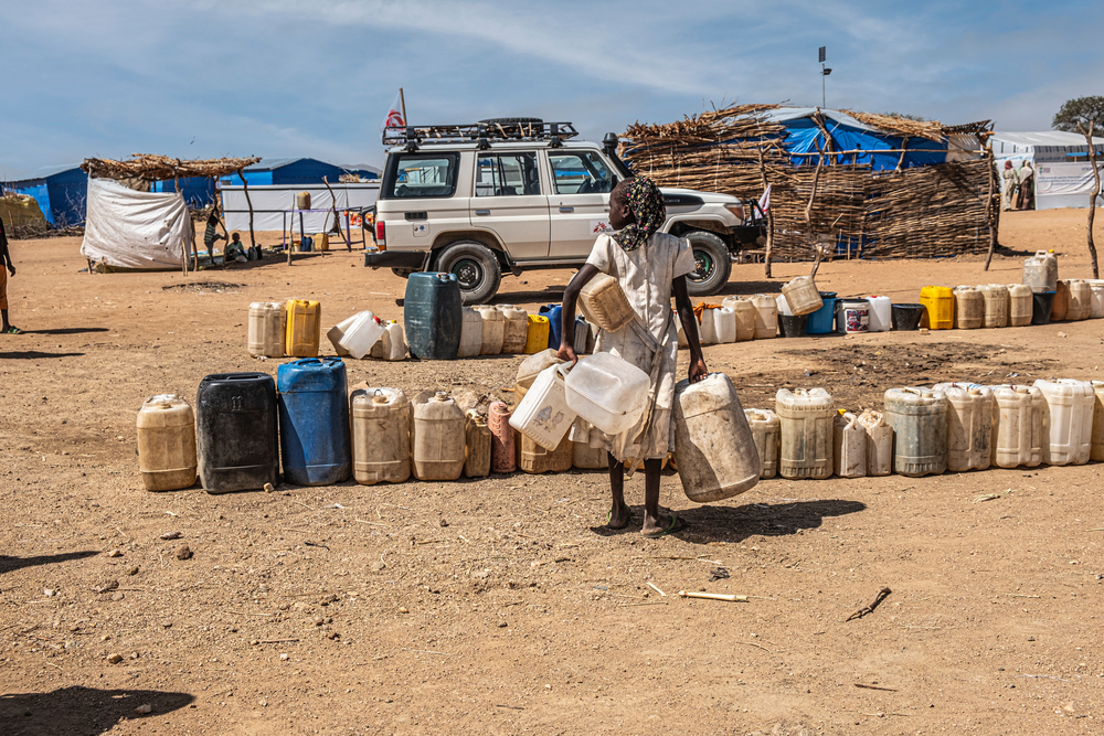 Person vor Wasserbehältern in Sandlandschaft