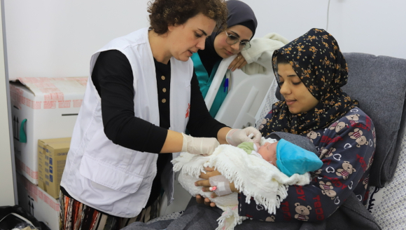 Mitarbeitende mit Patientin während Untersuchung von Neugeborenem