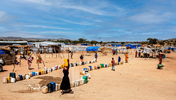 Camp aus Hütten in Wüste, dazwischen laufen Menschen