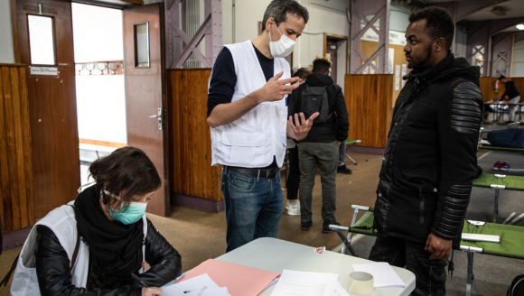 Ein Mitarbeiter von Ärzte ohne Grenzen im Gespräch mit einem der in der Turnhalle untergebrachten Menschen.