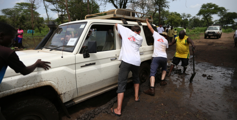 Bewohner eines Camps in Uganda helfen unserer Mitarbeitern, einen Wagen aus dem Matsch zu ziehen. Geflüchtete Uganda Teamarbeit Geländewagen