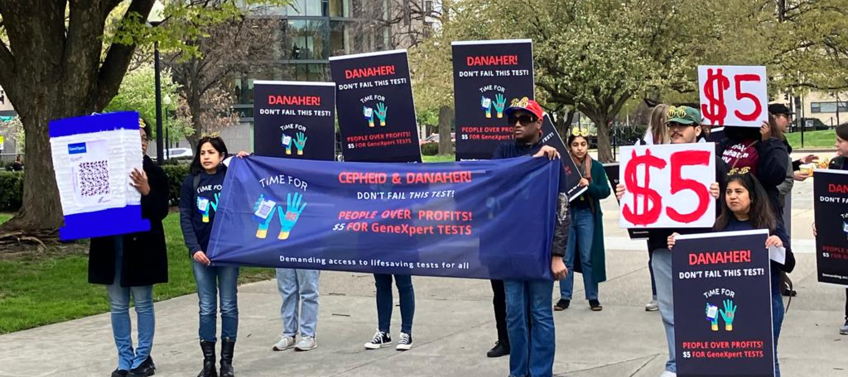 Gruppe Menschen hält Schilder mit Forderung an Danaher Preis zu senken