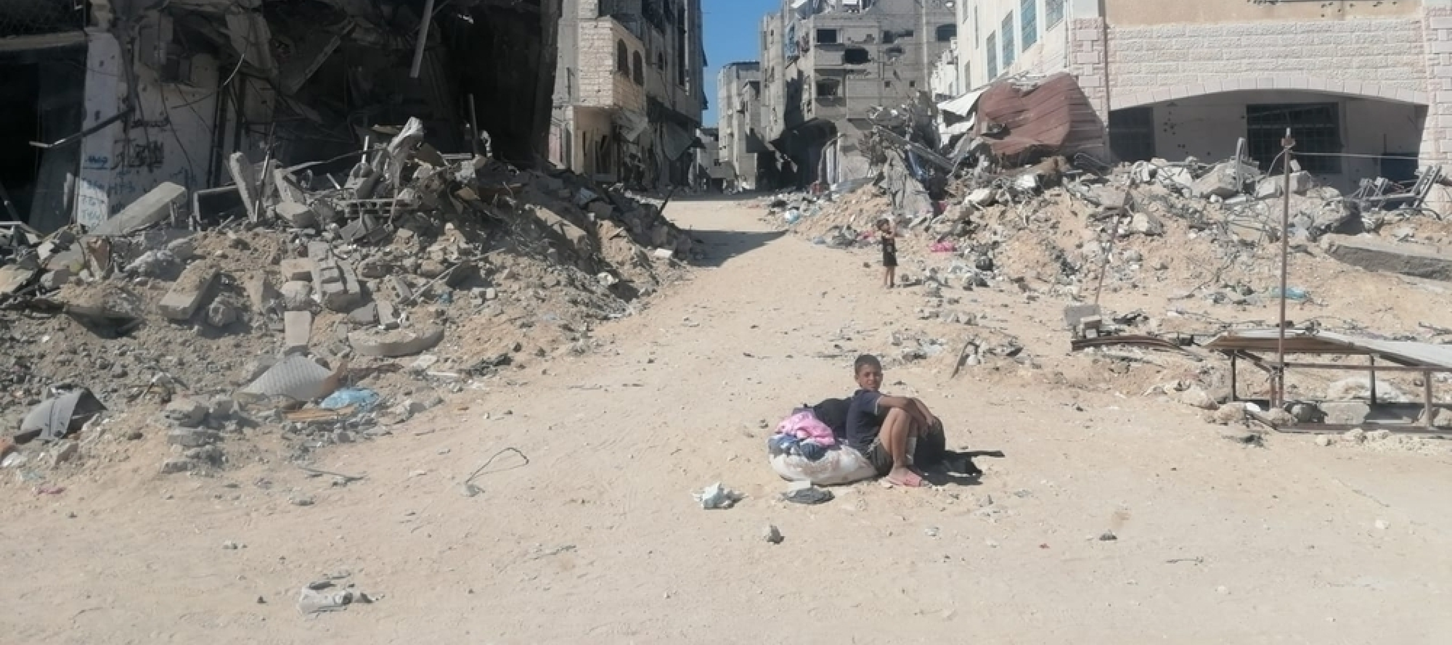 Junge sitzt auf Sandstraße in zerstörter Stadt