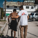 Ein Mitarbeiter von Ärzte ohne Grenzen stützt einen Mann auf Krücken