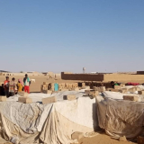 Menschen stehen in der Wüste Nigers auf einer offenen Fläche mit provisorischer Behausung.