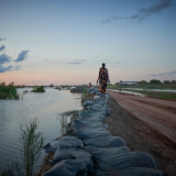 Frau läuft im Südsudan einen Deich enlang - Flutwasser ist überall.