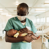 Ein Krankenpfleger in Sierra Leona hält ein Neugeborenes.
