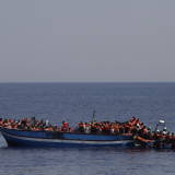 232 in Seenot geratene Menschen mit Rettungswesten auf einem Holzboot im Mittelmeer