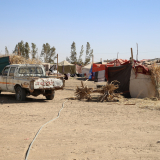 Ein altes Auto vor einem Camp mit vielen Zelten in einer wüstenähnlichen Landschaft