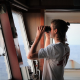 Ein Mitarbeiter von Ärzte ohne Grenzen steht auf einer Schiffsbrücke und schaut durch ein Fernglas.