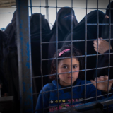 Ein Mädchen sieht durch den Zaun im Al-Hol Camp