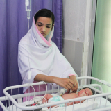 Krankenpflegerin behandelt Neugeborenes in Kinderbett